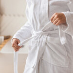 Wellness And Spa. Unrecognizable Woman Untying White Bathrobe Preparing For Beauty Ritual In Modern Bathroom In Hotel Or Spa Center. Female Body Care And Pampering. Cropped Shot